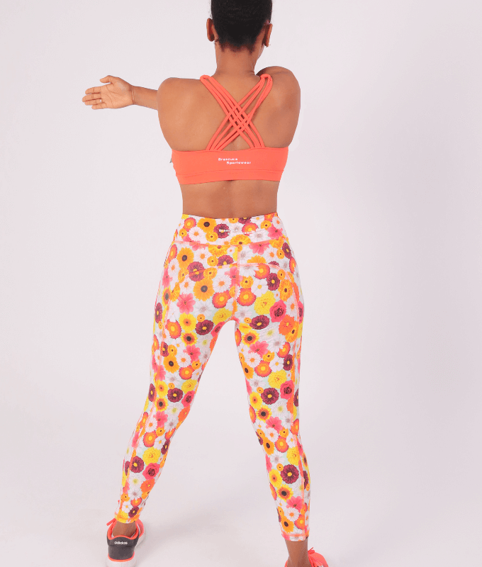 Leggings tobilleros tiro alto de estampado floral vibrante en tonos anaranjados y vino en fondo blanco y top con varios tirantes cruzados en la espalda en color naranja a juego.